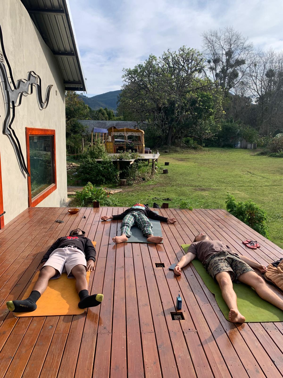 Yoga class in South Africa with students in savasana on outdoor deck surrounded by nature and mountains